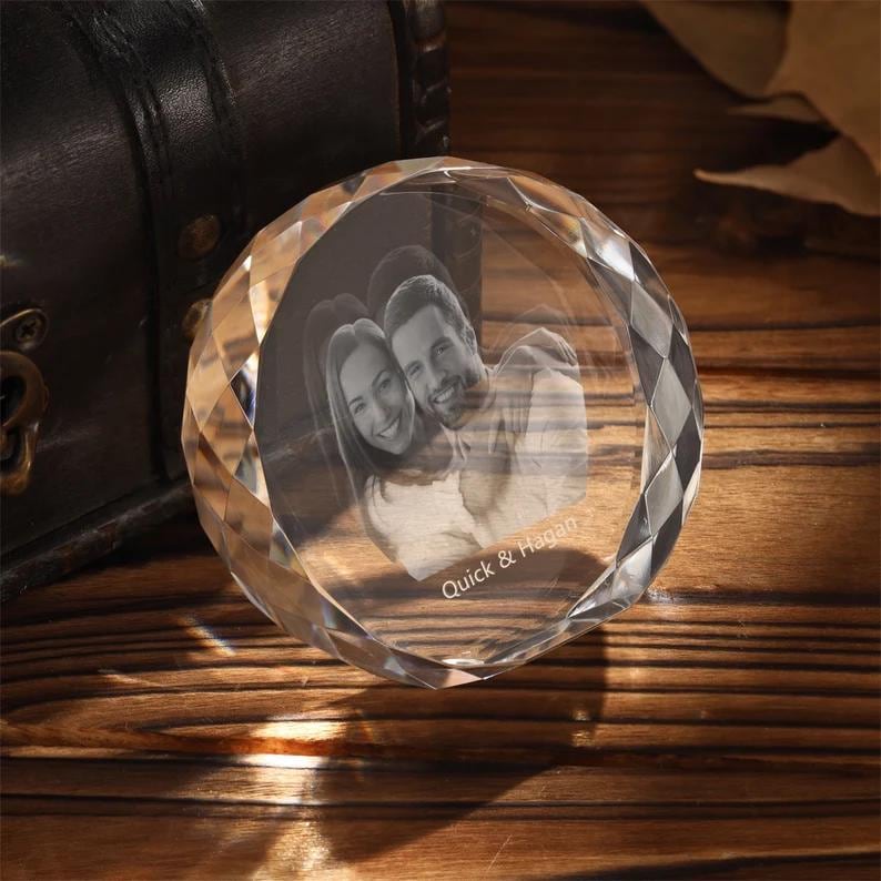 May include: A clear crystal paperweight with a 3D engraved image of a couple. The paperweight has a faceted design and the text "Quick & Hagan" is engraved on the bottom.