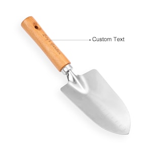 May include: A gardening trowel with a wooden handle and a stainless steel blade. The handle is light brown and has the text "Lily's Garden" printed on it. The blade is silver and has measurement markings.