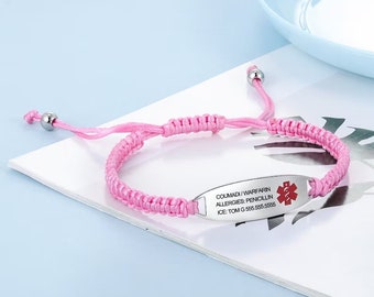 May include: Pink braided medical ID bracelet with a silver-tone metal plate. The plate has red medical symbol and text: COUMADI/WARFARIN, ALLERGIES: PENICILLIN, ICE: TOM G 555.555.5555. Adjustable cord closure.