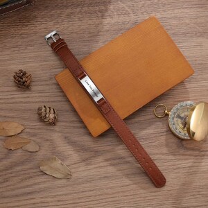 May include: A brown leather bracelet with a silver plate engraved with the words "Love You Forever".