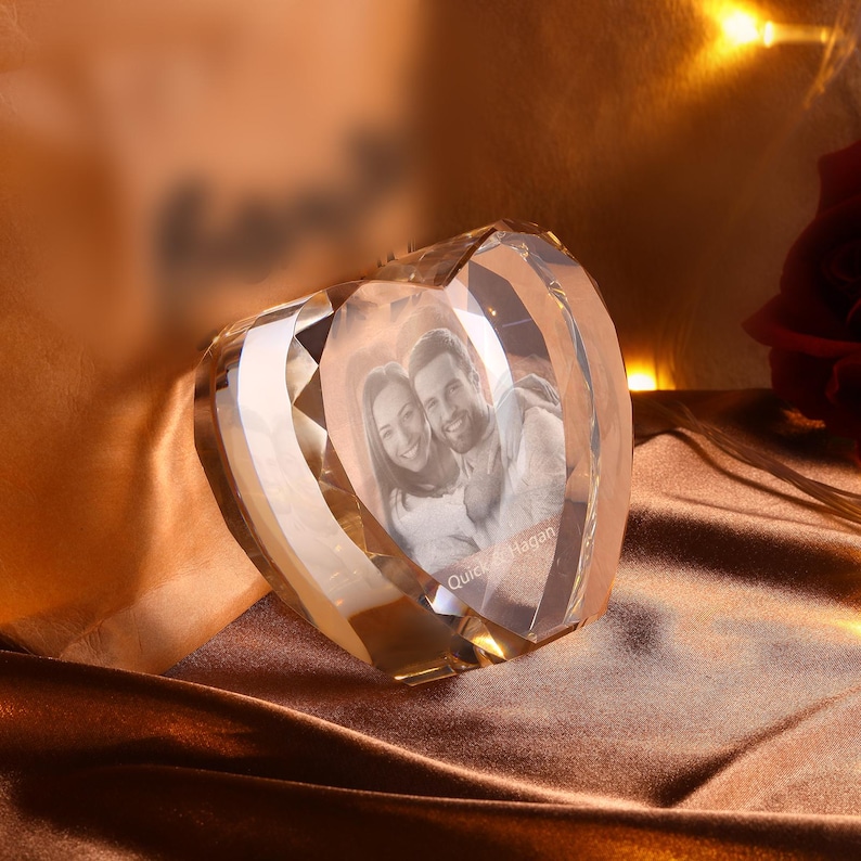 May include: A crystal heart shaped paperweight with a 3D engraved image of a couple inside. The couple is smiling and the text "Quick & Hagan" is engraved below them.
