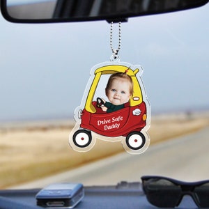 May include: A red and yellow toy car rearview mirror charm with a child's face in the driver's seat. The car has the words "Drive Safe Daddy" on the side.