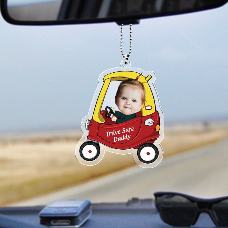 May include: A red and yellow toy car rearview mirror charm with a child's face in the driver's seat. The car has the words "Drive Safe Daddy" on the side.