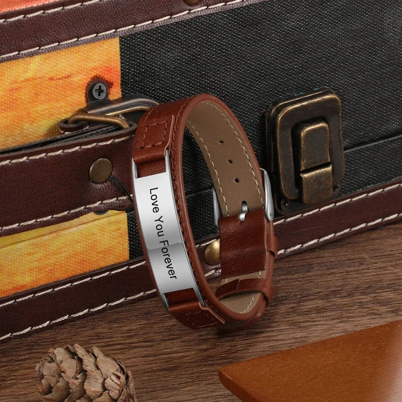 May include: A brown leather bracelet with a silver plate engraved with the words "Love You Forever".