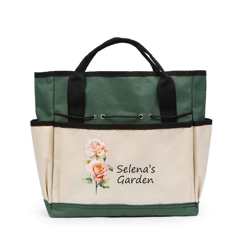 May include: A gardening tote bag with a green top and black handles. The front of the bag is beige with a watercolor image of roses and the text "Selena's Garden". The bag has multiple pockets and a drawstring closure.