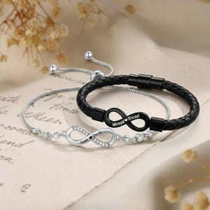 Può includere: Due braccialetti infinity personalizzati. Uno è in argento con i nomi "Smith" e "David" incisi. L'altro è in pelle nera con i nomi "Mireyal" e "Ericayl" incisi. Entrambi i braccialetti hanno un simbolo infinito.