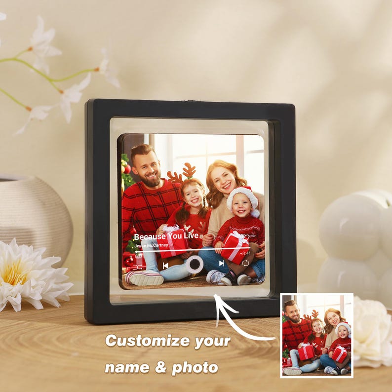 May include: A square black floating frame containing a photograph of a family of four wearing red holiday sweaters. The photo features a music player interface overlay with the text Because You Live by Jesse McCartney and a progress bar.