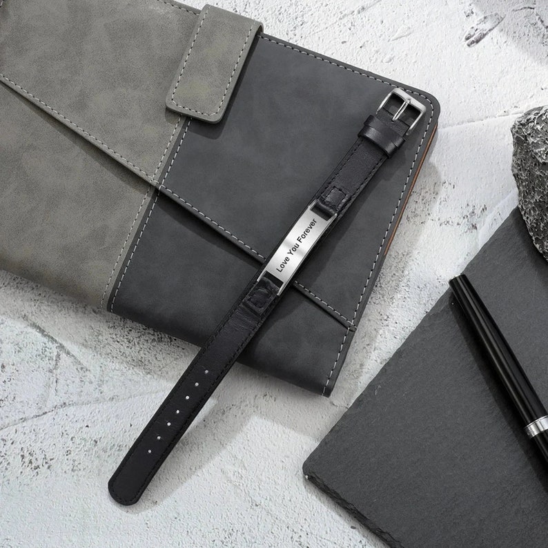 May include: A black leather bracelet with a silver plate engraved with the words "Love You Forever".