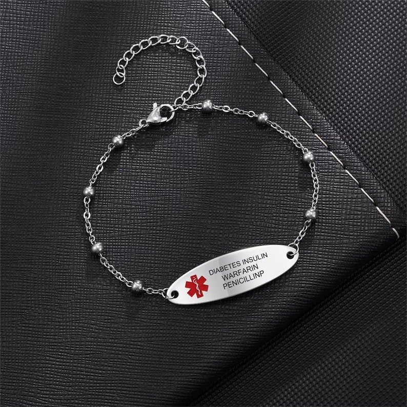 May include: A silver medical alert bracelet with a red star of life symbol and the text "DIABETES INSULIN WARFARIN PENICILLIN".