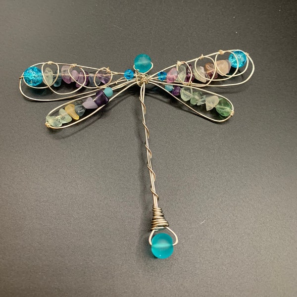 Dragonfly with purples, pinks, greens and swirled wire on the wings.