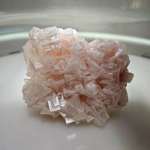 May include: A close-up of a pinkish-white mineral specimen. The crystalline structure is visible, with many small, square-shaped crystals clustered together. The mineral has a slightly translucent appearance.