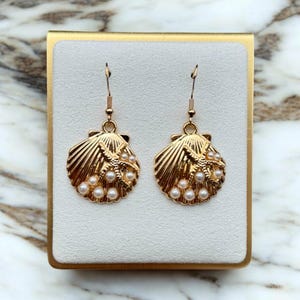 May include: Gold tone earrings with a seashell design and pearl accents. The seashells have a starfish design in the centre.