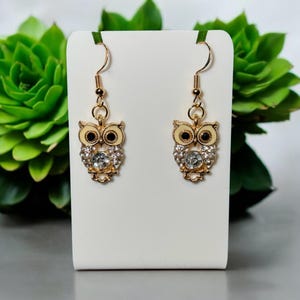 May include: Gold owl dangle earrings with clear rhinestones and a white enamel finish.