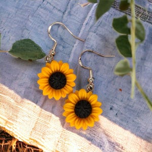 May include: A pair of sunflower earrings with gold hooks. The sunflowers are yellow with black centres.