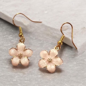 May include: A pair of gold dangle earrings with pink flower charms. The flowers have a white centre and a gold outline.