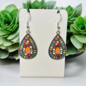 May include: A pair of teardrop-shaped dangle earrings with a silver finish. The earrings are decorated with colorful beads and a central orange bead.