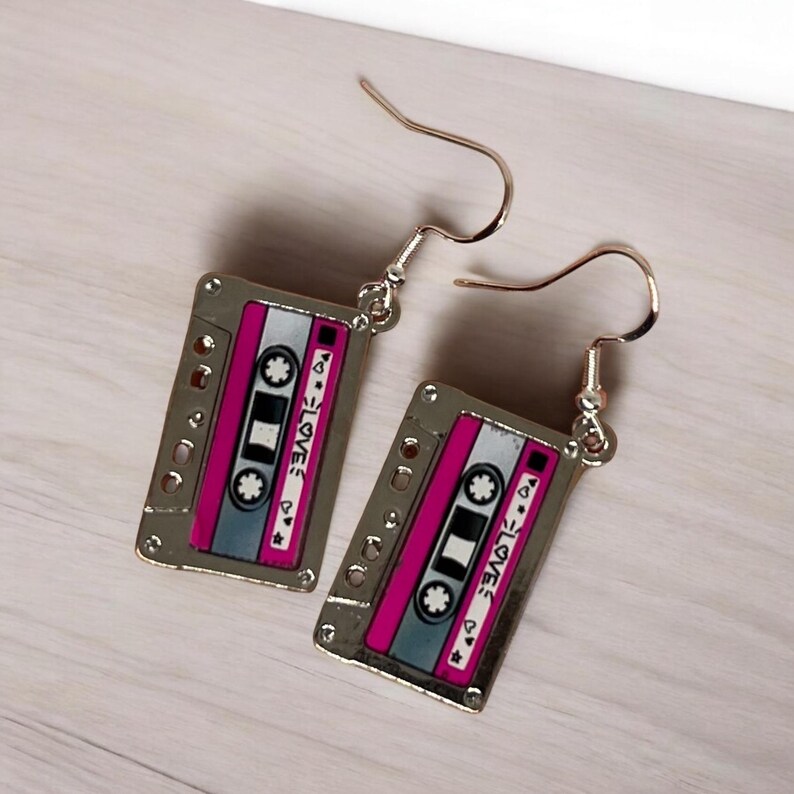 May include: A pair of silver cassette tape earrings with pink and gray details. The tape has the word "LOVE" written on it.