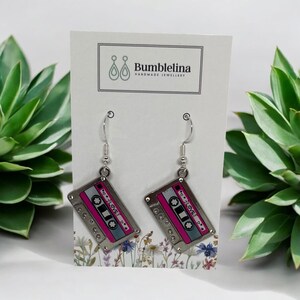 May include: Silver dangle earrings with a pink and silver cassette tape charm. The charm has the text "I &hearts; LOVE" on it.