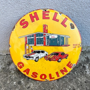 Puede incluir: Letrero redondo vintage de Shell Gasoline con fondo amarillo y letras rojas. El letrero presenta una ilustración de la gasolinera Shell, dos coches clásicos y el texto "Made in USA '55".