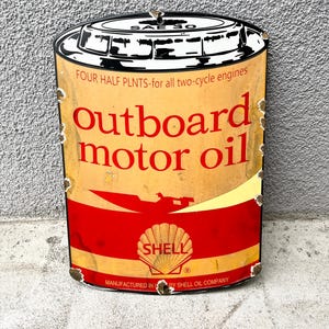 Puede incluir: Un letrero de metal de estilo vintage con forma de lata de aceite de motor con un esquema de color amarillo y rojo. Presenta el texto SAE 30, FOUR HALF PLNTS-for all two-cycle engines, outboard motor oil y el logotipo de Shell con el texto SHELL.