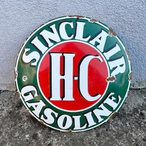 Puede incluir: Letrero redondo de Sinclair Gasoline con borde verde y texto blanco. El centro presenta un círculo rojo con letras blancas "HC". El letrero tiene un aspecto vintage desgastado con óxido visible.