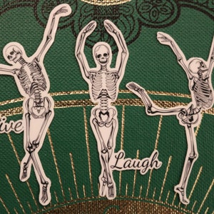 Op de afbeelding: Drie skeletfiguren in een dansende pose met de woorden "Live", "Laugh" en "Love" onder elke figuur.