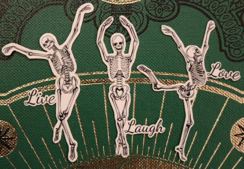 Op de afbeelding: Drie skeletfiguren in een dansende pose met de woorden "Live", "Laugh" en "Love" onder elke figuur.