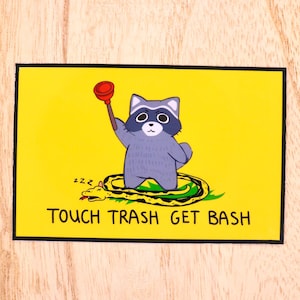 May include: A yellow and black sticker with a cartoon raccoon holding a plunger and a snake. The text on the sticker reads "Touch Trash Get Bash".
