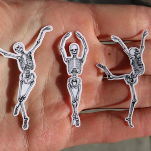 Op de afbeelding: Drie zwart-witte skelet stickers op een hand. De skeletten staan in verschillende poses, &eacute;&eacute;n staat met de armen omhoog, &eacute;&eacute;n staat met de armen gespreid en &eacute;&eacute;n staat met &eacute;&eacute;n been omhoog.