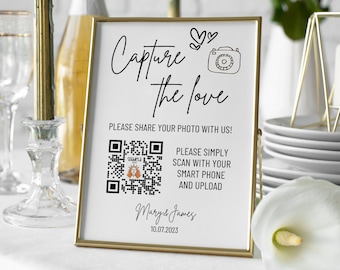Könnte beinhalten: Ein goldfarbener Rahmen mit weißem Hintergrund und schwarzem Text, der "Capture the love" lautet. Das Schild zeigt außerdem ein Herz, ein Kamerasymbol und einen QR-Code. Der Text unter dem QR-Code lautet "Bitte einfach mit Ihrem Smartphone scannen und hochladen" und "Mary & James 10.07.2023".