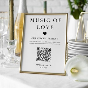 Op de afbeelding: Een gouden lijst met de tekst "MUSIC OF LOVE" en een zwart hartje. Onder de tekst staat een QR-code en de tekst "OUR WEDDING PLAYLIST" gevolgd door "As we embark on this incredible journey of love, we're excited to share the soundtrack of our hearts with you." Het bord bevat ook de namen "MARY & JAMES" en de datum "10.07.2025".