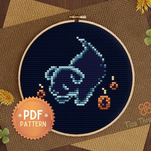May include: A cross-stitch pattern in a wooden embroidery hoop. The design features a stylized ghost with jack-o'-lanterns in shades of blue and orange on a dark blue background. A PDF pattern sticker is in the lower left.