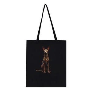 Puede incluir: Bolso tote negro con una ilustración detallada de un perro con joyas doradas. El perro está sentado sobre un fondo negro. El bolso tote tiene asas negras.