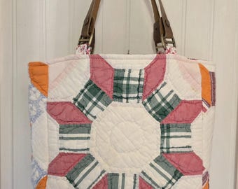 May include: A quilted tote bag featuring a patchwork star pattern in shades of pink, green, and white. The bag has two brown leather handles attached with metal hardware and a white fabric lining visible at the top near the handle attachments.