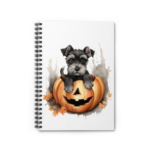 Könnte beinhalten: Spiralgebundenes Notizbuch mit einer Aquarellillustration eines schwarz-grauen Welpen in einem geschnitzten orangefarbenen Kürbis. Der Kürbis hat ein Halloween-Gesicht. Herbstblätter und graue Aquarellspritzer vervollständigen das Halloween-Design.