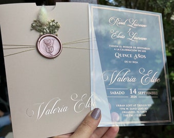 May include: A clear acrylic invitation with gold lettering for a Quinceañera. The invitation reads "Ranel Laureano and Eladis Laureano have the honor of inviting you to the celebration of the Quince Años of their daughter Valeria Elise. Saturday, September 14, 2024. Urban Loft at Trellis 925, 7594 W. Sand Lake Rd, Orlando, FL 32819. 7:00 PM - 12:00 AM."
