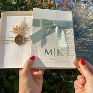Une boîte d'invitation en ruban vert sauge qui peut être spécialement préparée pour vos événements. Faire-part en acrylique, enveloppe en parchemin, fleurs séchées