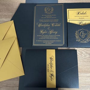 Invitación de boda dorada. Invitación acrílica con impresión en lámina dorada. Bolsillo negro perlado, cinturón estampado. Sobre de envío y tarjeta de detalles.