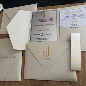 Zilveren gespiegelde, parel ivoorkleurige zakuitnodigingsset. Zwart en goud bedrukt. Zakriemdetail en postenvelop. Met detailkaarten