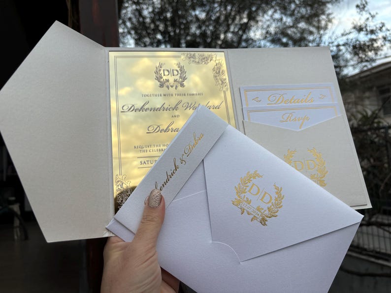 May include: A white wedding invitation with gold foil accents. The invitation features the couple's names, "Dokendrick & Dobra", and the date of the wedding. The invitation also includes a gold foil monogram with the initials "DD".