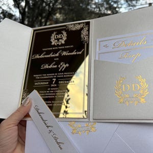 May include: A white and gold wedding invitation with a mirror finish. The invitation features the names "Dokendrick Woodard" and "Debra Eppp" with the date "Saturday 7 December 2024".