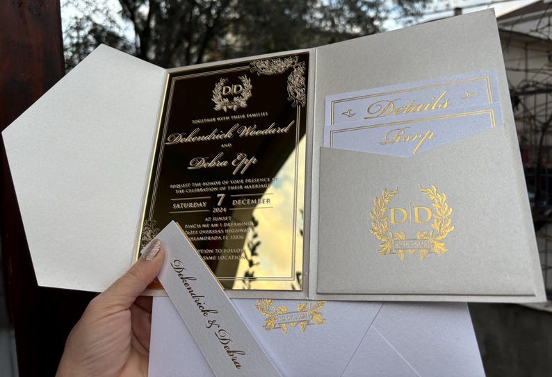 May include: A white and gold wedding invitation with a mirror finish. The invitation features the names "Dokendrick Woodard" and "Debra Eppp" with the date "Saturday 7 December 2024".