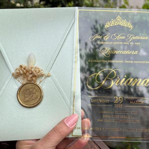 Invitación de quinceañera en acrílico transparente. Sobre verde pistacho claro perlado. Invitación con corona. Invitación en acrílico con estampado dorado.