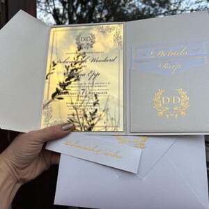 May include: A white and gold wedding invitation with a pocket for a RSVP card. The invitation features a gold floral design and the text "Dokeylog Woodard and Sierra Epp" with the date "7 December 2023".