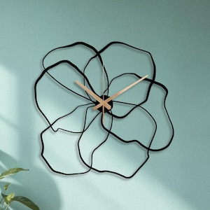 Peut inclure: Une horloge murale dotée d'un cadre en métal noir en forme de fleur abstraite avec des contours de pétales irréguliers et superposés. L'horloge possède deux aiguilles en bois clair positionnées au centre, contrastant avec la structure métallique.