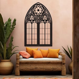 May include: A black, gothic-style window wall decor with intricate detailing. The window is mounted on a pink wall above a woven sofa with orange pillows. A matching orange rug and potted plants complete the room's decor.