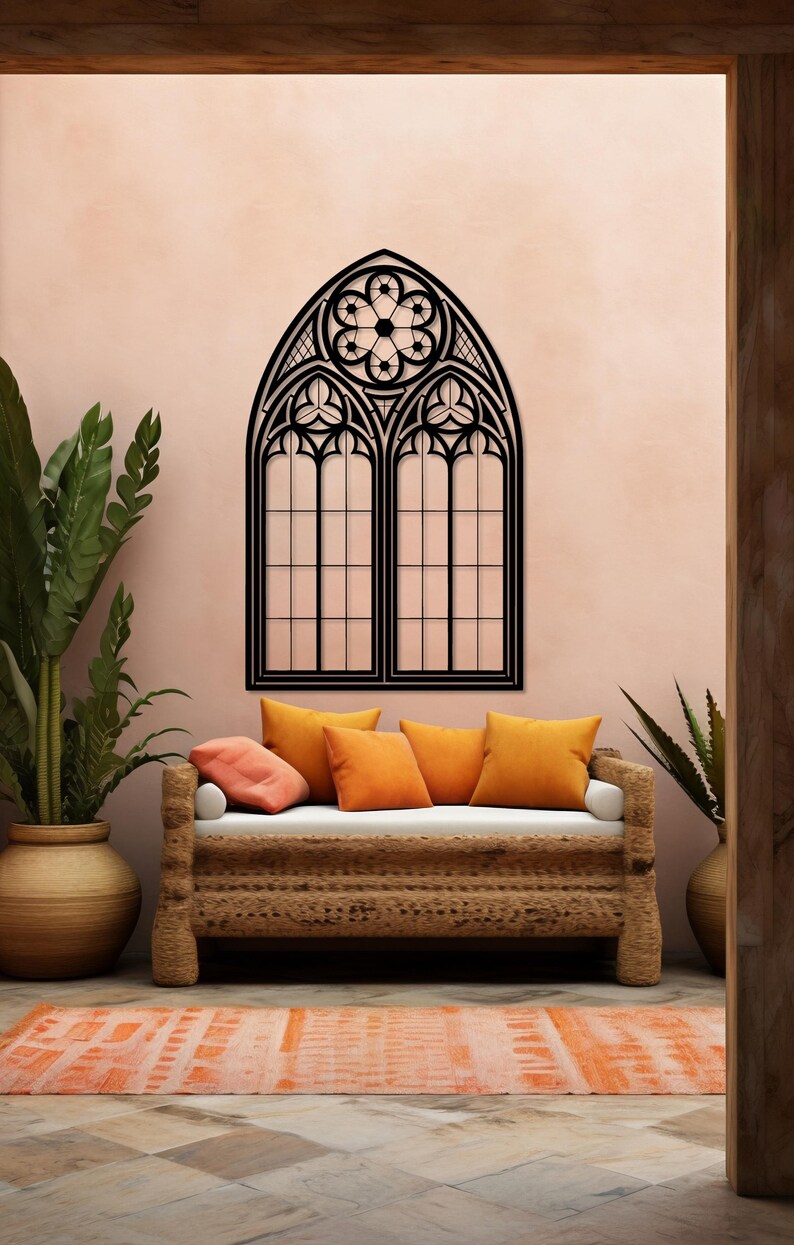 May include: A black, gothic-style window wall decor with intricate detailing. The window is mounted on a pink wall above a woven sofa with orange pillows. A matching orange rug and potted plants complete the room's decor.
