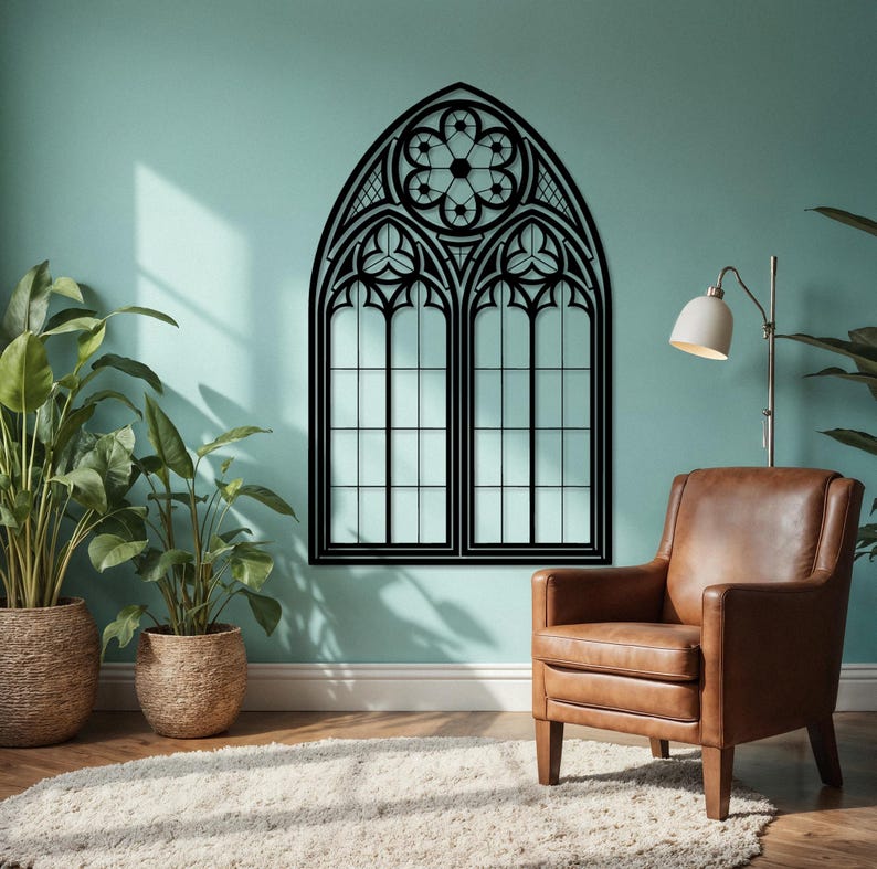 May include: A black, gothic-style window wall decor piece. The design features an arched top with intricate floral and geometric patterns. The window has two panes with a grid pattern, creating a striking contrast against the light-colored wall.