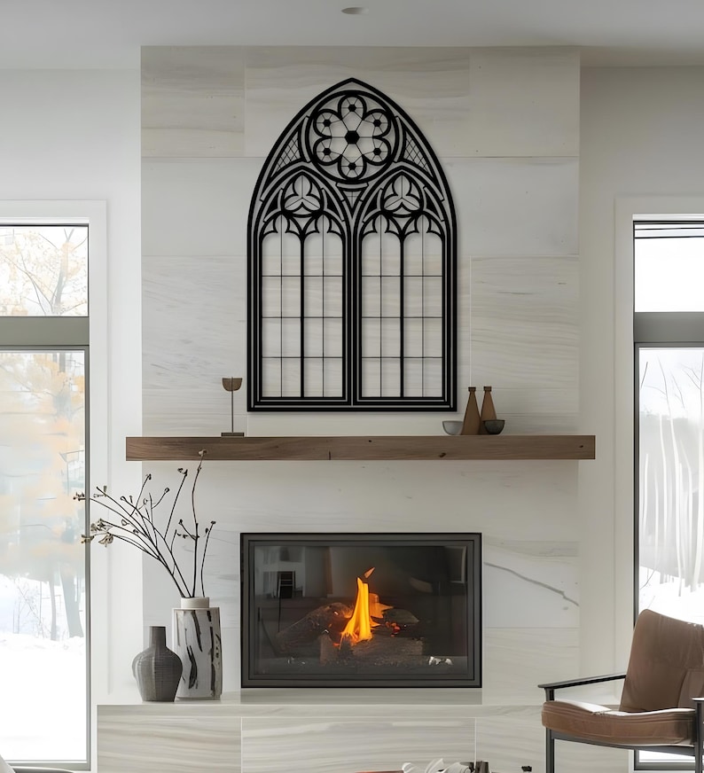 May include: A large, black metal wall art piece in the shape of a gothic cathedral window. The artwork features intricate geometric designs and a central rose window. It is mounted on a white marble wall above a wooden mantel.