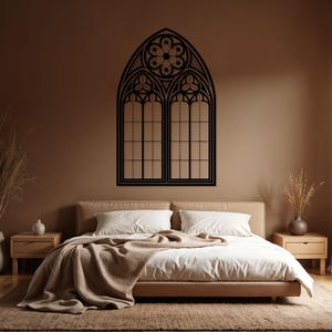 May include: Black, gothic-style window wall art. The decorative piece features an arched top with a floral design and two rectangular window panels. The artwork is mounted on a brown wall above a bed with white bedding.